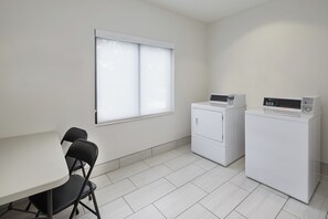A laundry room with two washing machines, a table, and chairs. - Holiday Inn Express Pensacola West - Navy Base by IHG (Pensacola)