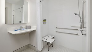 A modern bathroom with a shower, a sink with a mirror, and a small stool. - Holiday Inn Express Pensacola West - Navy Base by IHG (Pensacola)