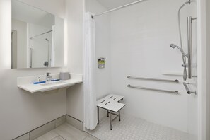 Un baño moderno con ducha, lavabo con espejo y un taburete pequeño.