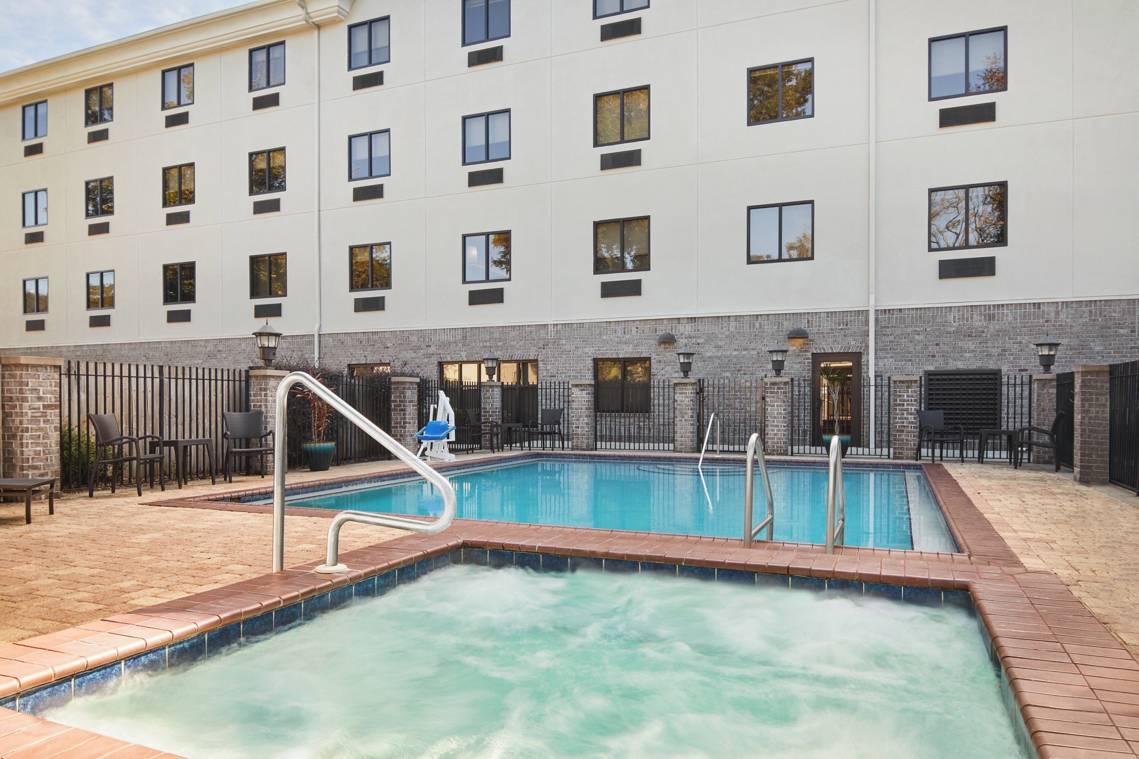 A hotel with a swimming pool, outdoor seating, and a brick wall.