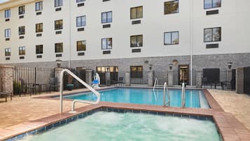 A hotel with a swimming pool, outdoor seating, and a brick wall.