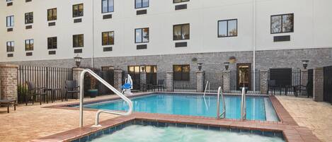 A hotel with a swimming pool, outdoor seating, and a brick wall.