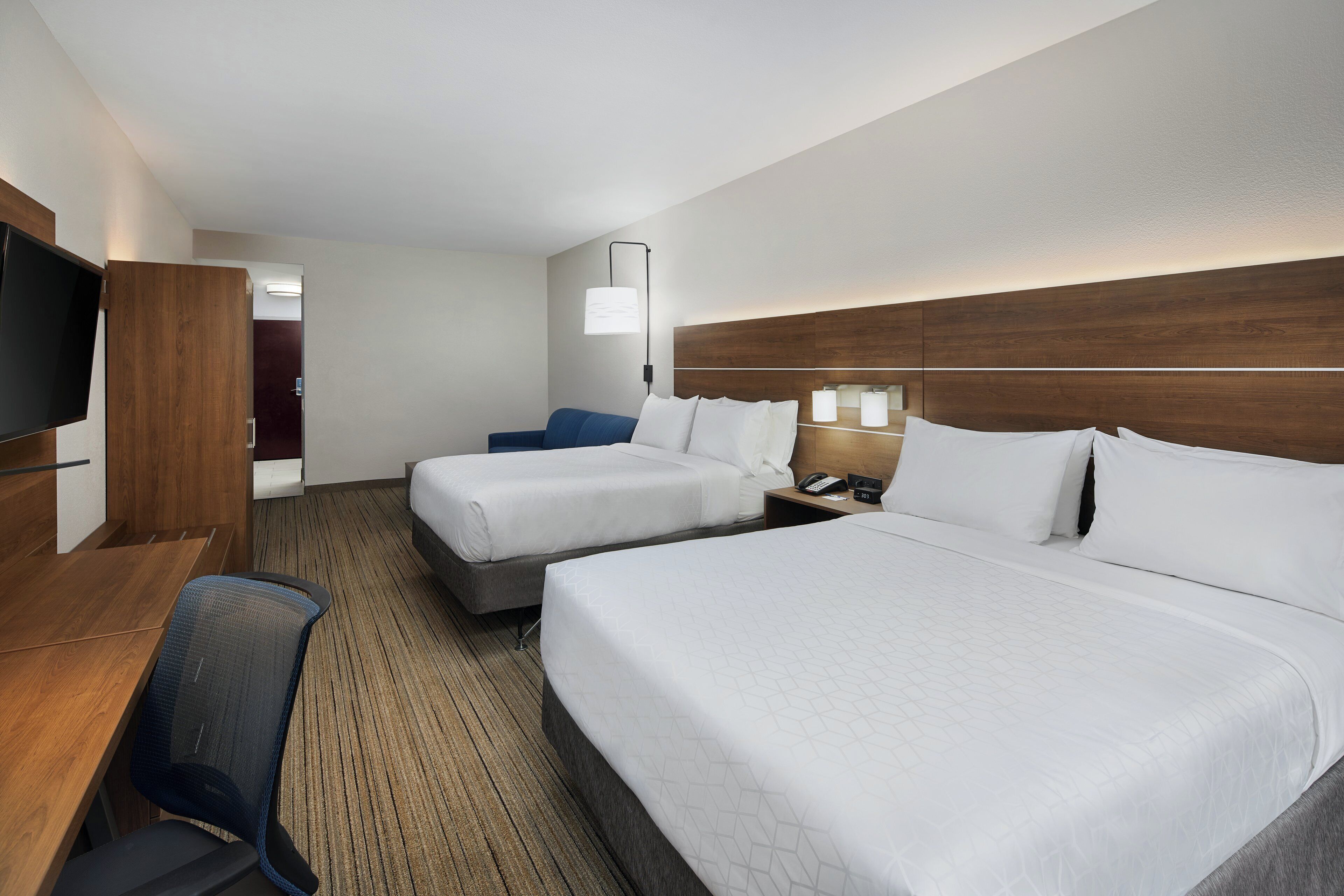 Une chambre d’hôtel avec deux lits, un bureau, une chaise, une télévision et une table de chevet avec une lampe.