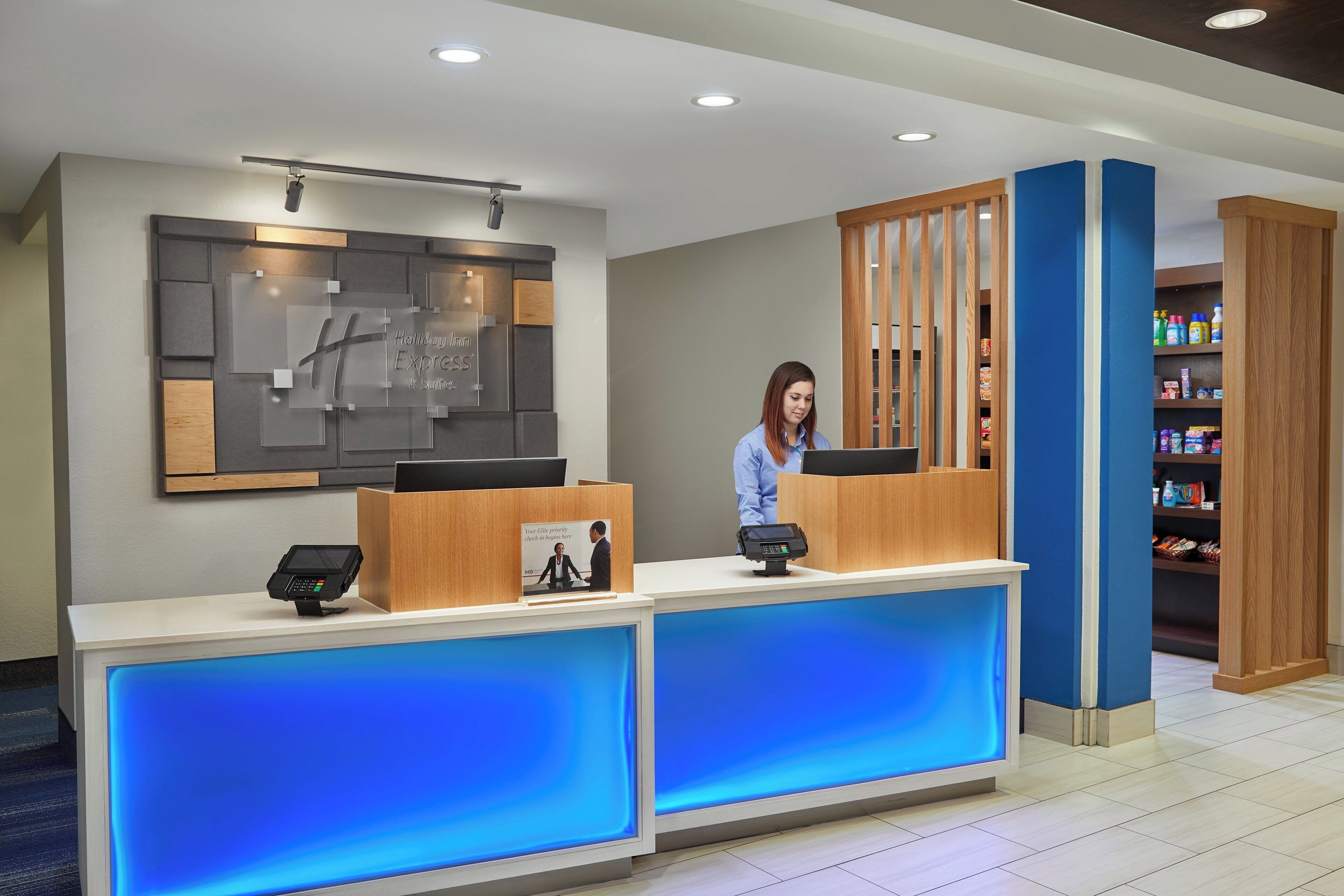 A hotel reception desk with a digital check-in kiosk, a large framed sign, and a blue-lit counter.