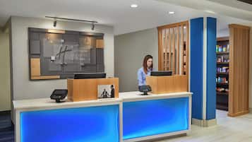A hotel reception desk with a digital check-in kiosk, a large framed sign, and a blue-lit counter.