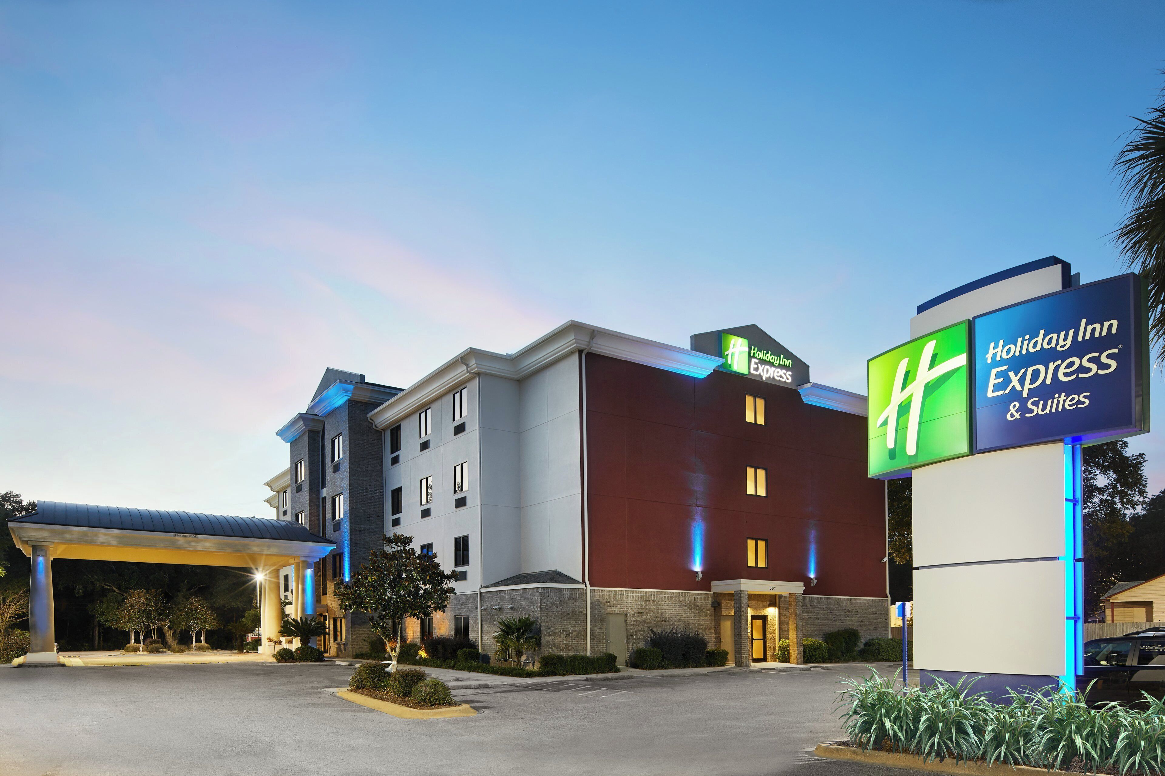 A Holiday Inn Express & Suites hotel with a modern design, featuring a prominent sign, a covered parking area, and a well-maintained landscape.