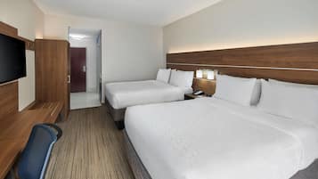 A hotel room with two beds, a desk with a chair, a TV, and a wooden headboard.