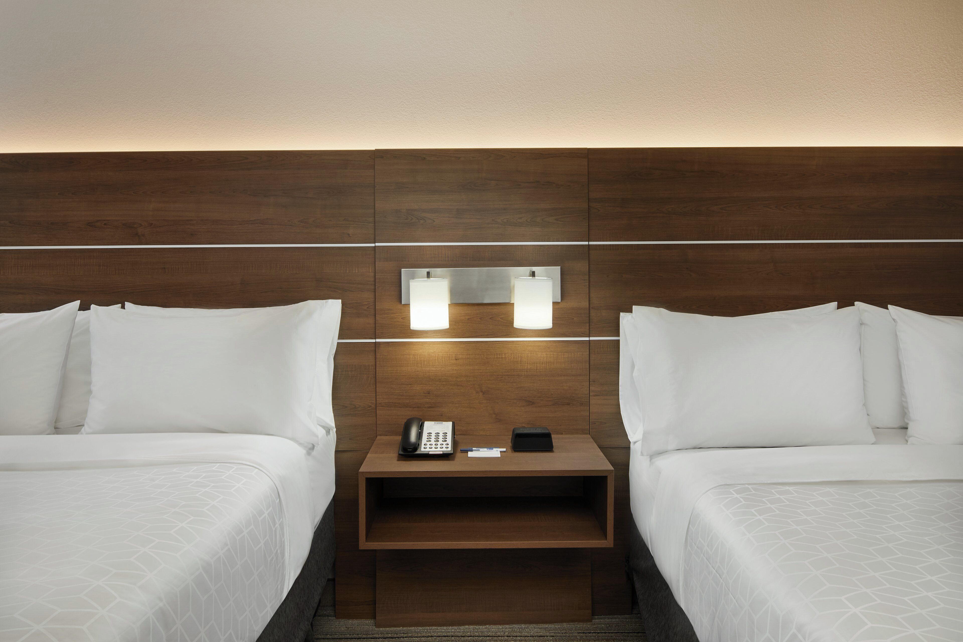 Habitación de hotel con dos camas, una mesita de noche con teléfono y libreta, y un espejo colgado en la pared.