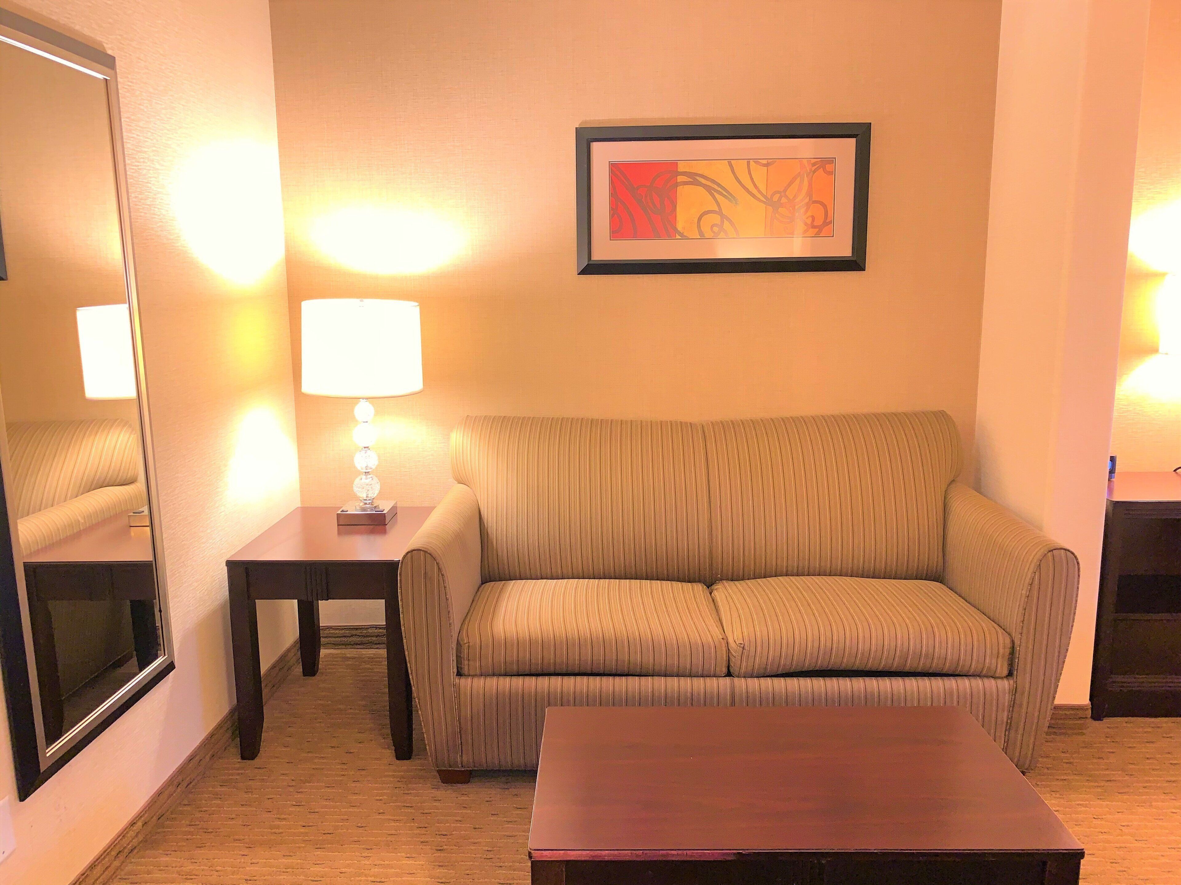 A living room with a sofa, a coffee table, a lamp, a framed picture on the wall, and a mirror on the wall.