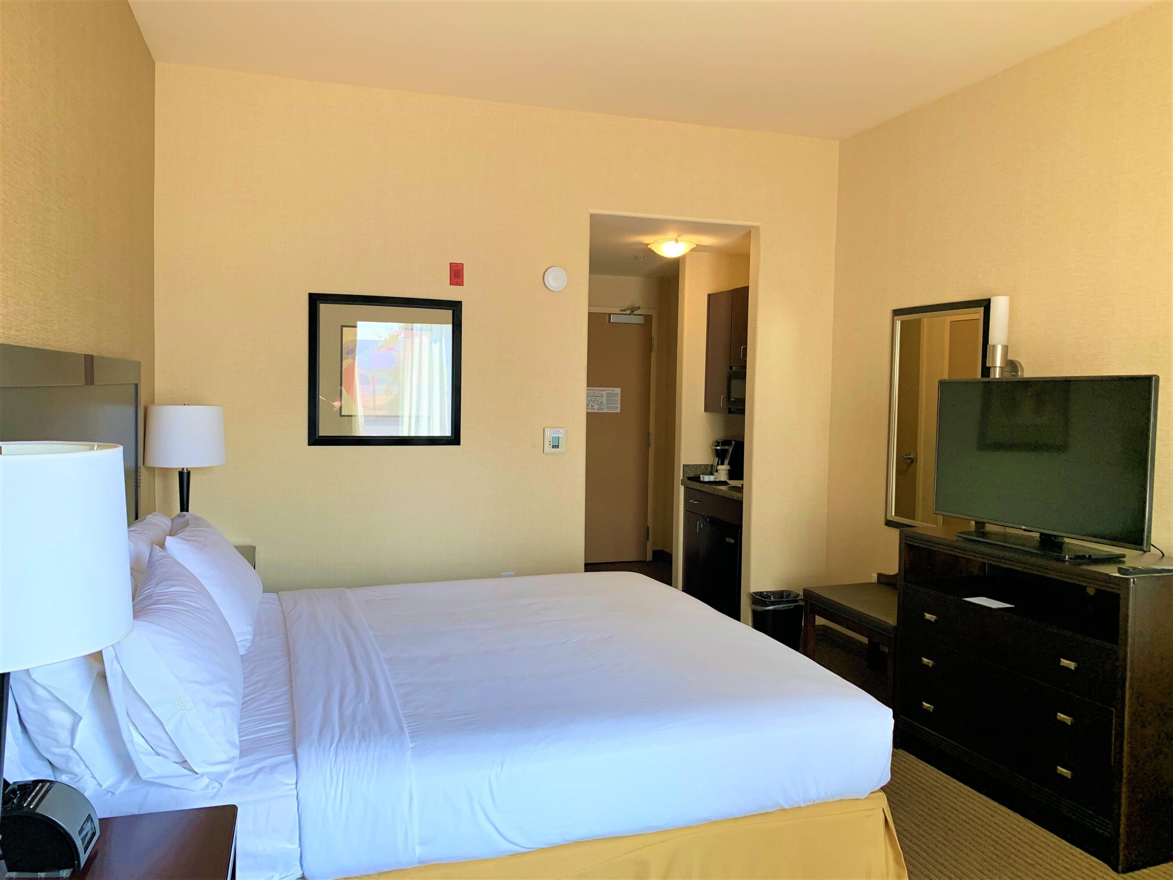 A hotel room with a bed, a television, a desk with a lamp, and a dresser.