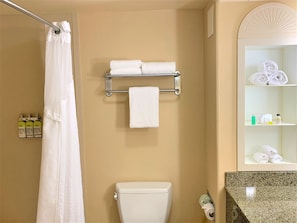 Une salle de bain équipée d’une douche, de toilettes, d’un porte-serviettes et d’étagères contenant des articles de toilette.