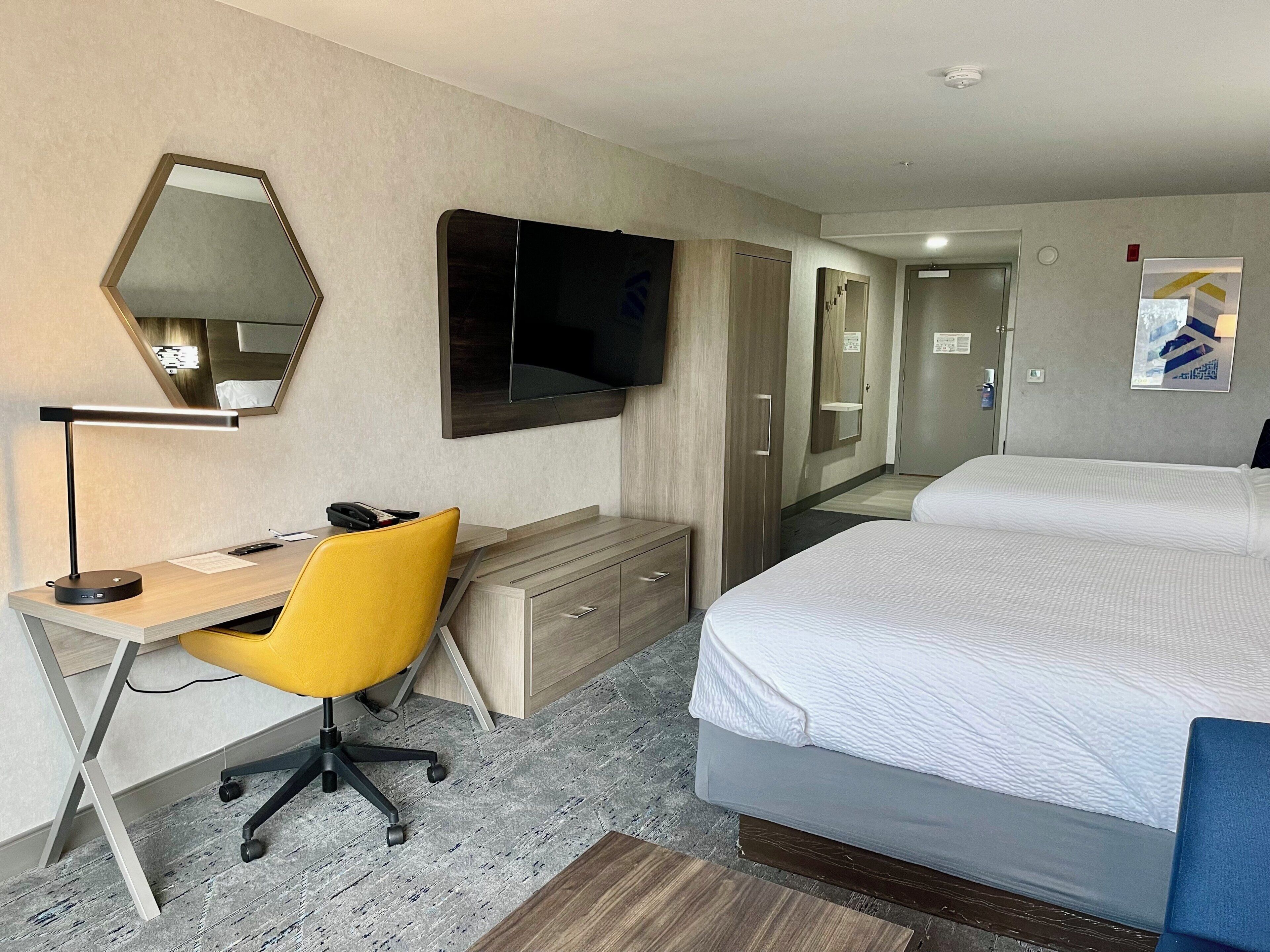 Une chambre d’hôtel équipée d’un bureau, d’une chaise, d’un lit et d’un téléviseur fixé au mur.