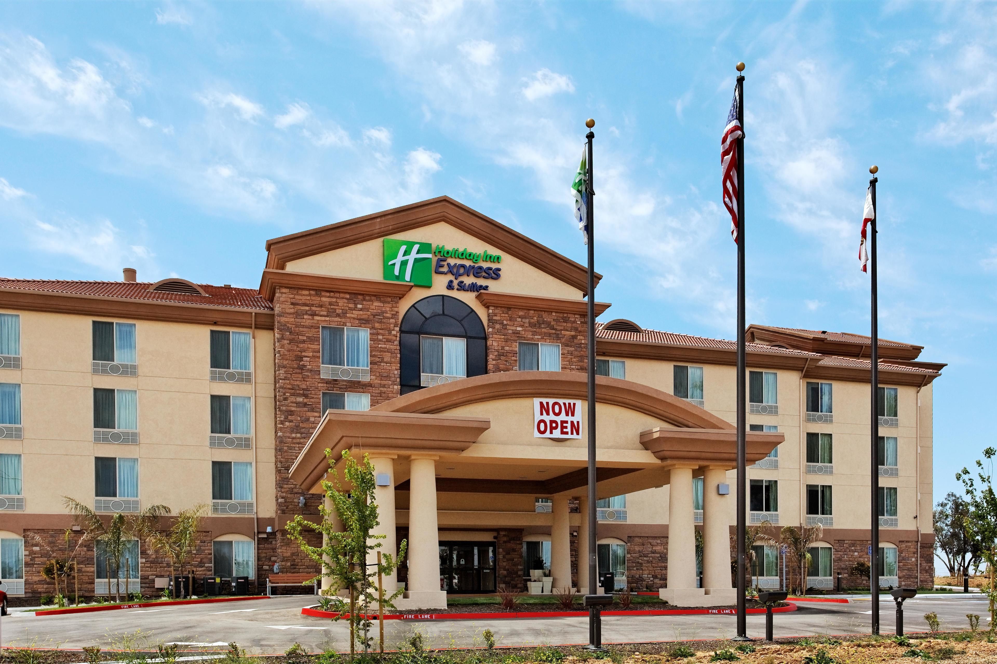 Un hotel Holiday Inn Express & Suites con un letrero que dice 'ABIERTO' que presenta fachada de ladrillo, múltiples ventanas y entrada ajardinada.