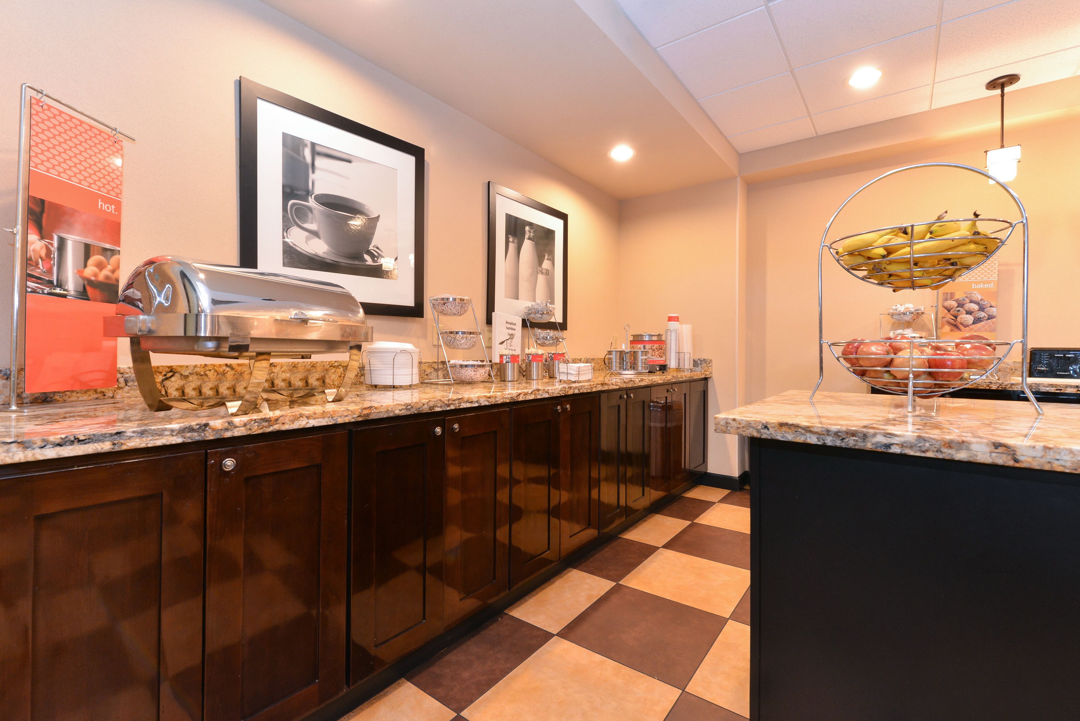 A kitchen with a coffee station, a fruit bowl, and framed pictures on the wall.