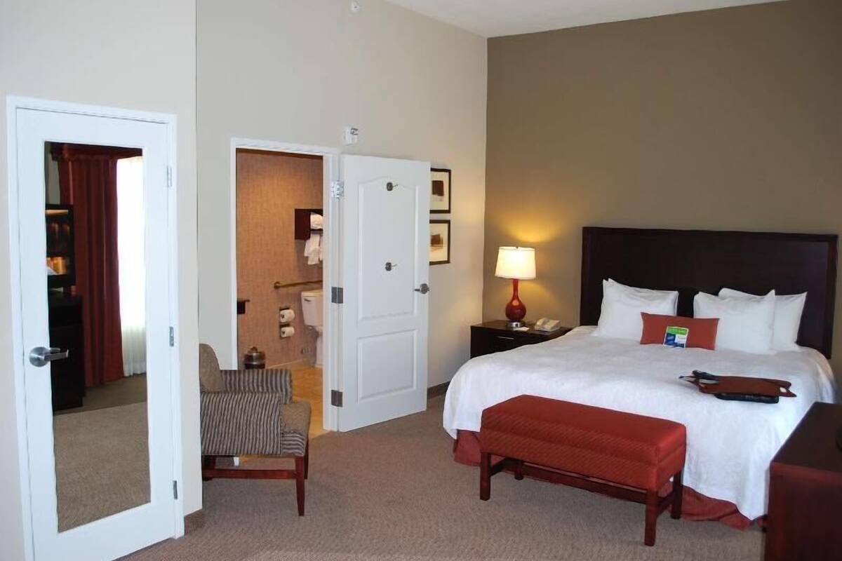 Une chambre d’hôtel comprenant un lit, une table de chevet, une chaise, une lampe et une porte donnant sur une autre pièce.