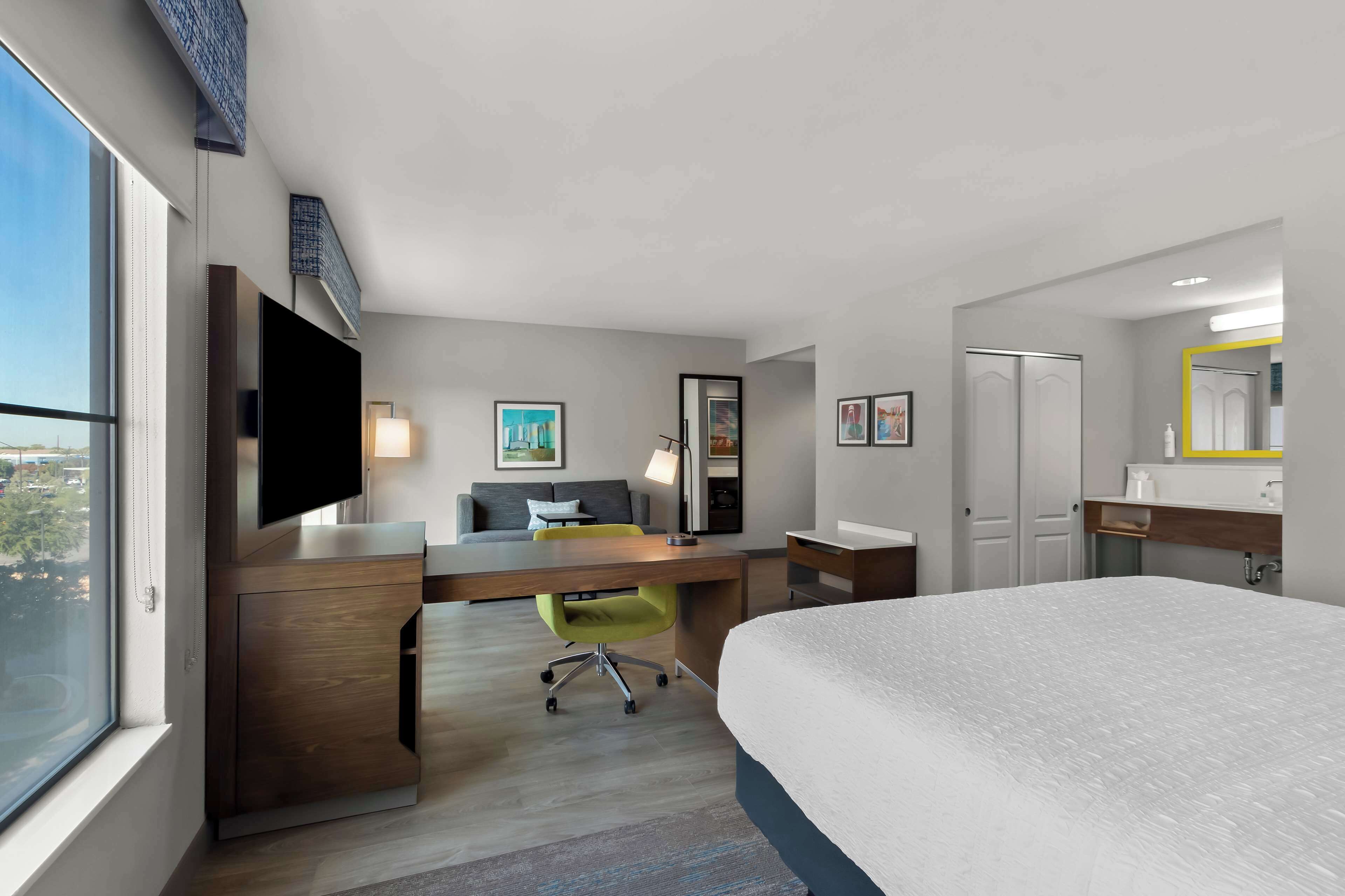 Una habitación de hotel moderna con una cama grande, un escritorio con silla, un televisor y una ventana con vista a la ciudad.