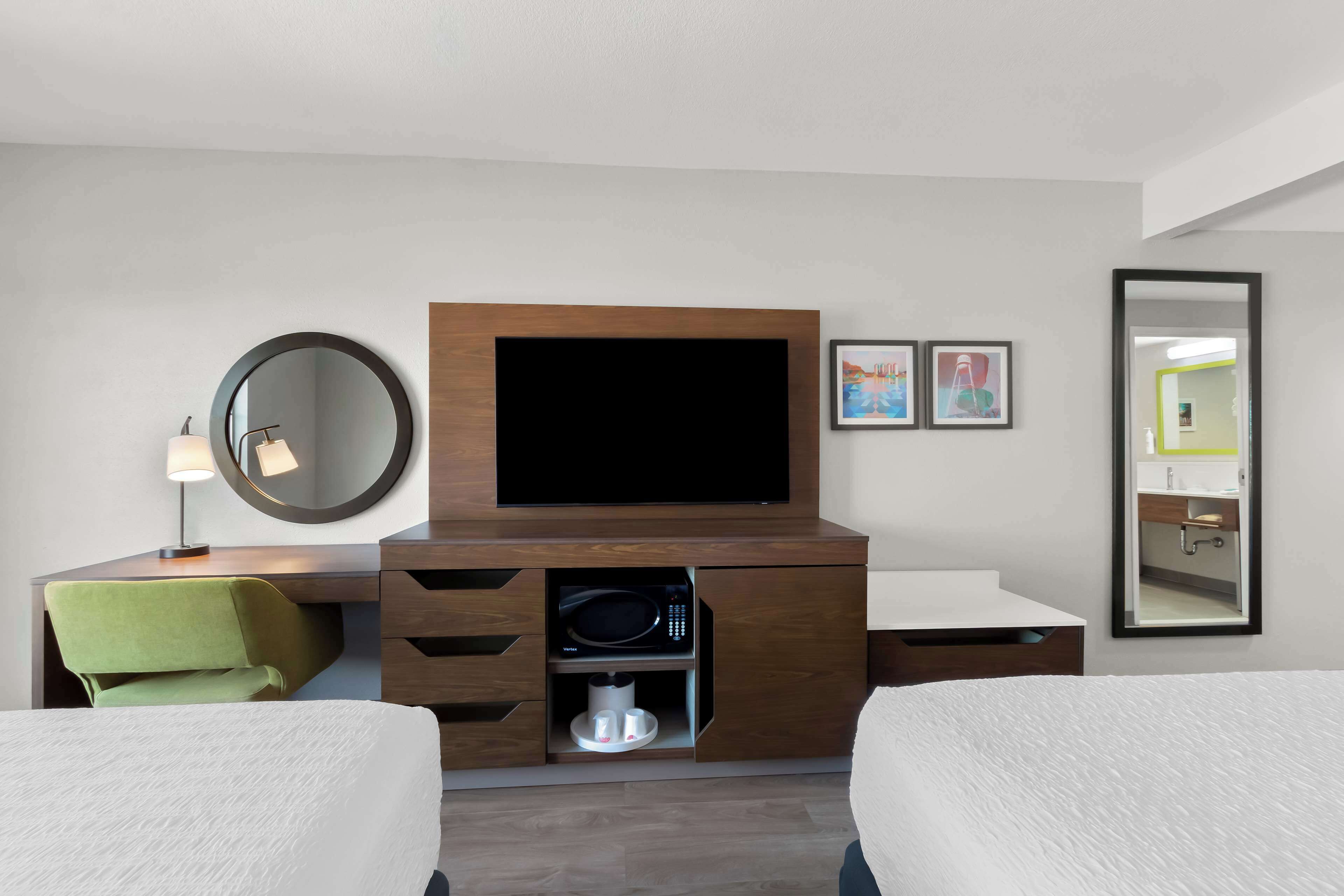 A hotel room with a bed, a desk with a lamp, a TV, a microwave, and a mirror.