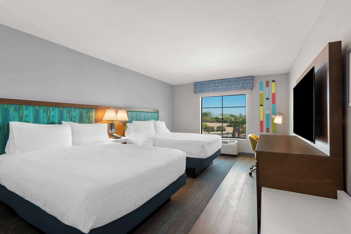 Une chambre d’hôtel avec deux lits, un bureau, une télévision et une grande fenêtre donnant sur un beau paysage.