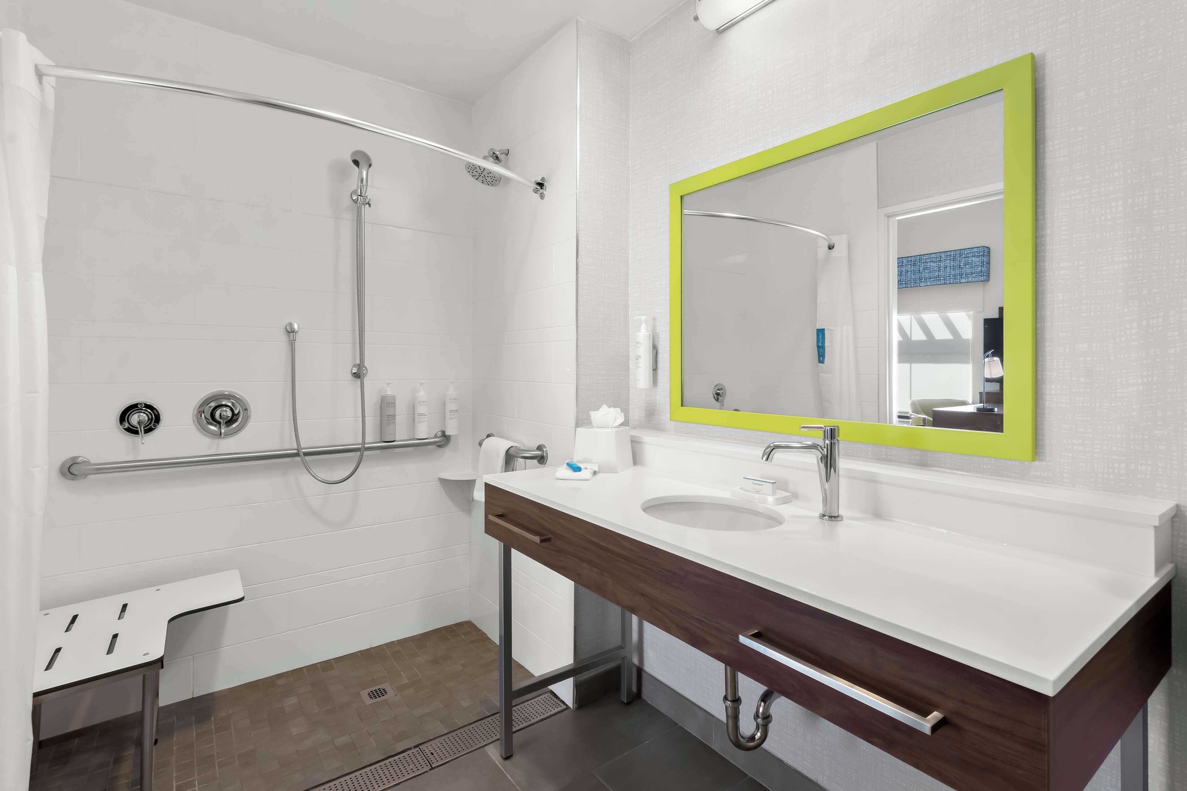 Un baño moderno con ducha, lavamanos con espejo y un perchero para toallas.