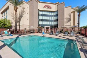 A hotel with a swimming pool, outdoor seating, and palm trees.