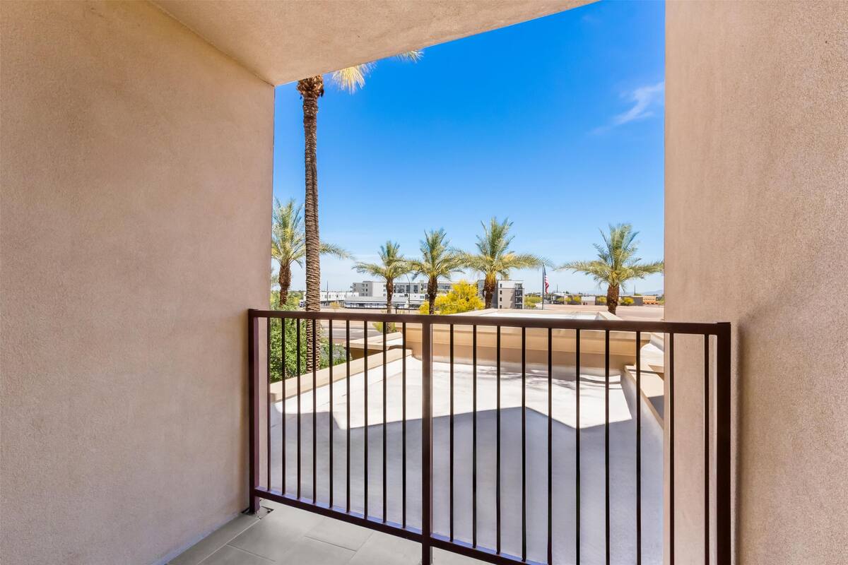 Un balcon avec une balustrade en métal, un ciel d’un bleu limpide et des palmiers en arrière-plan.