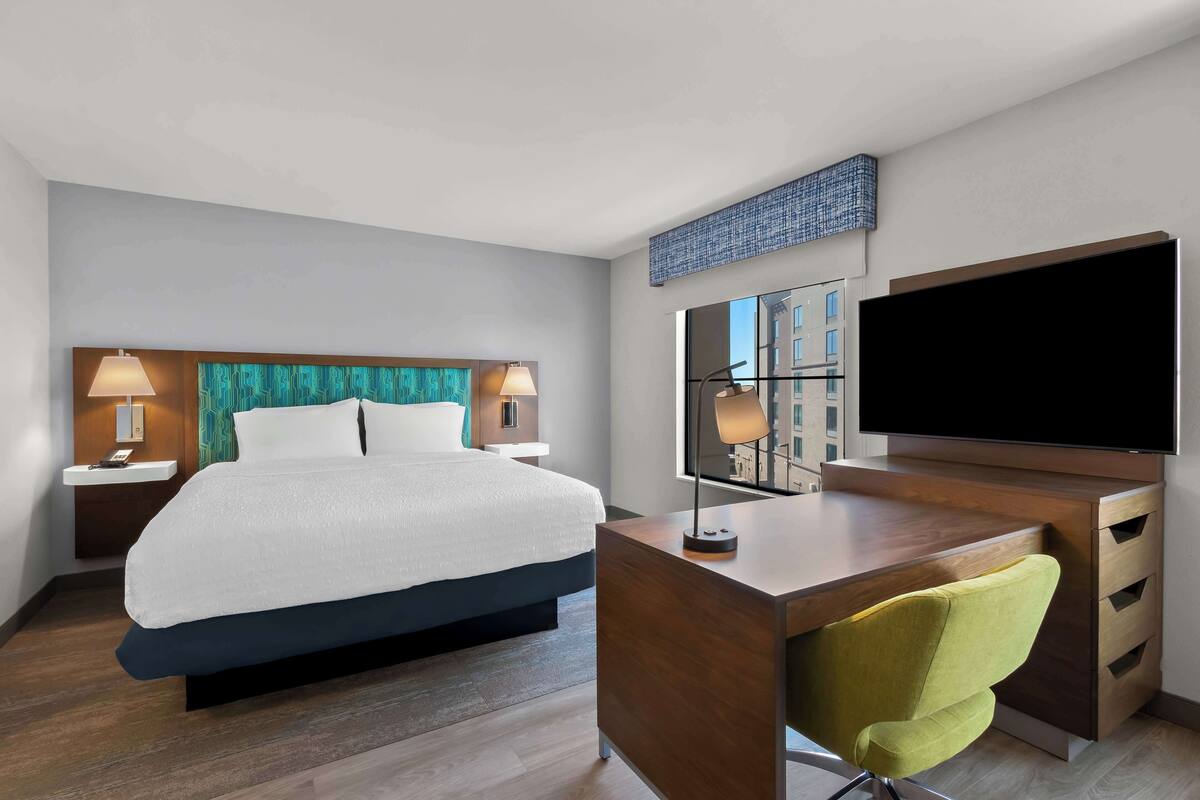 Une chambre d’hôtel moderne dotée d’un grand lit, d’un bureau avec une chaise, d’une télévision à écran plat et d’une grande fenêtre.