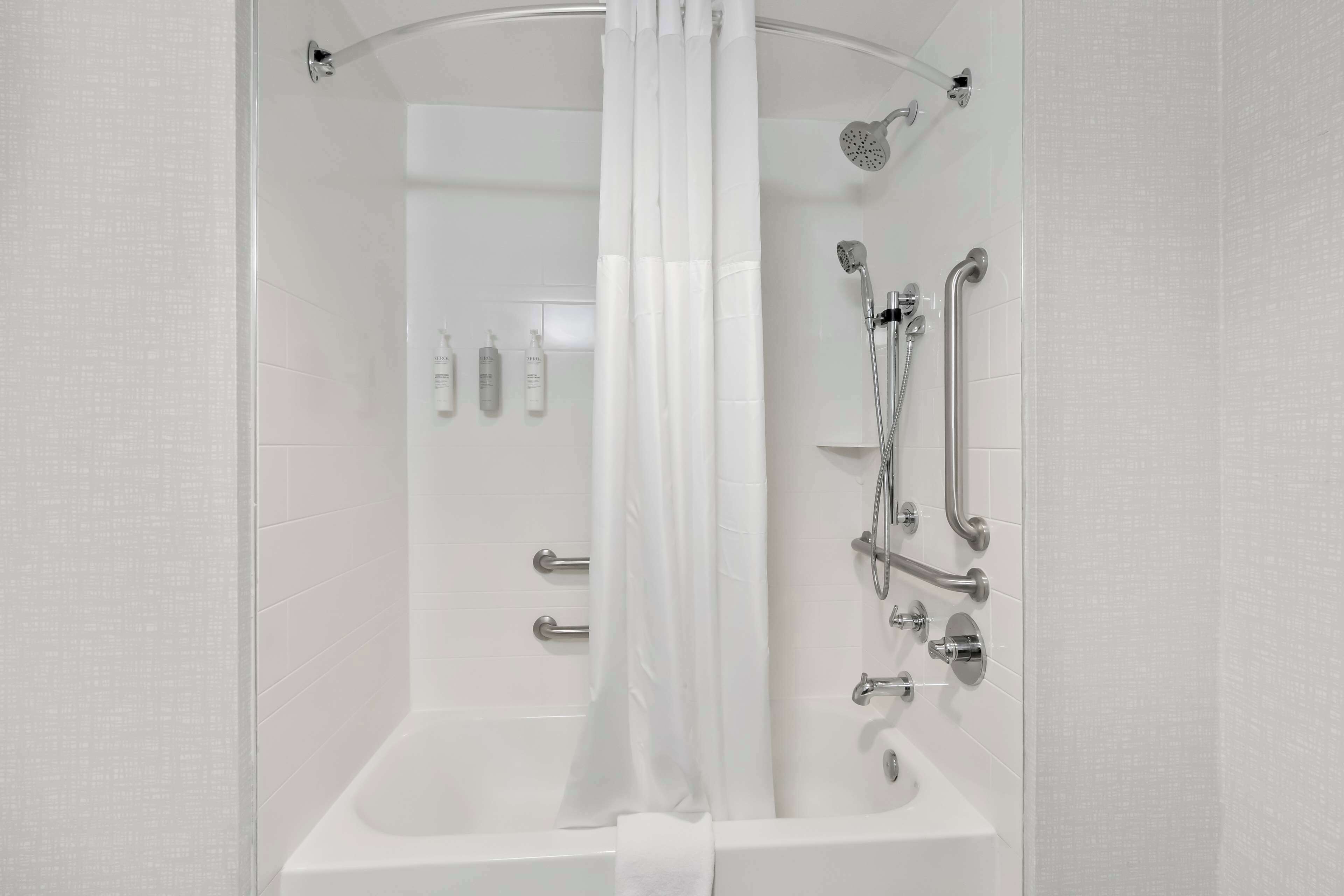 A modern bathroom with a walk-in shower, grab bars, and a glass partition.