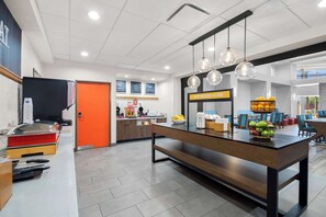 A modern kitchen with a central island, a bright orange door, and a 'Happy Breakfast Here' sign.