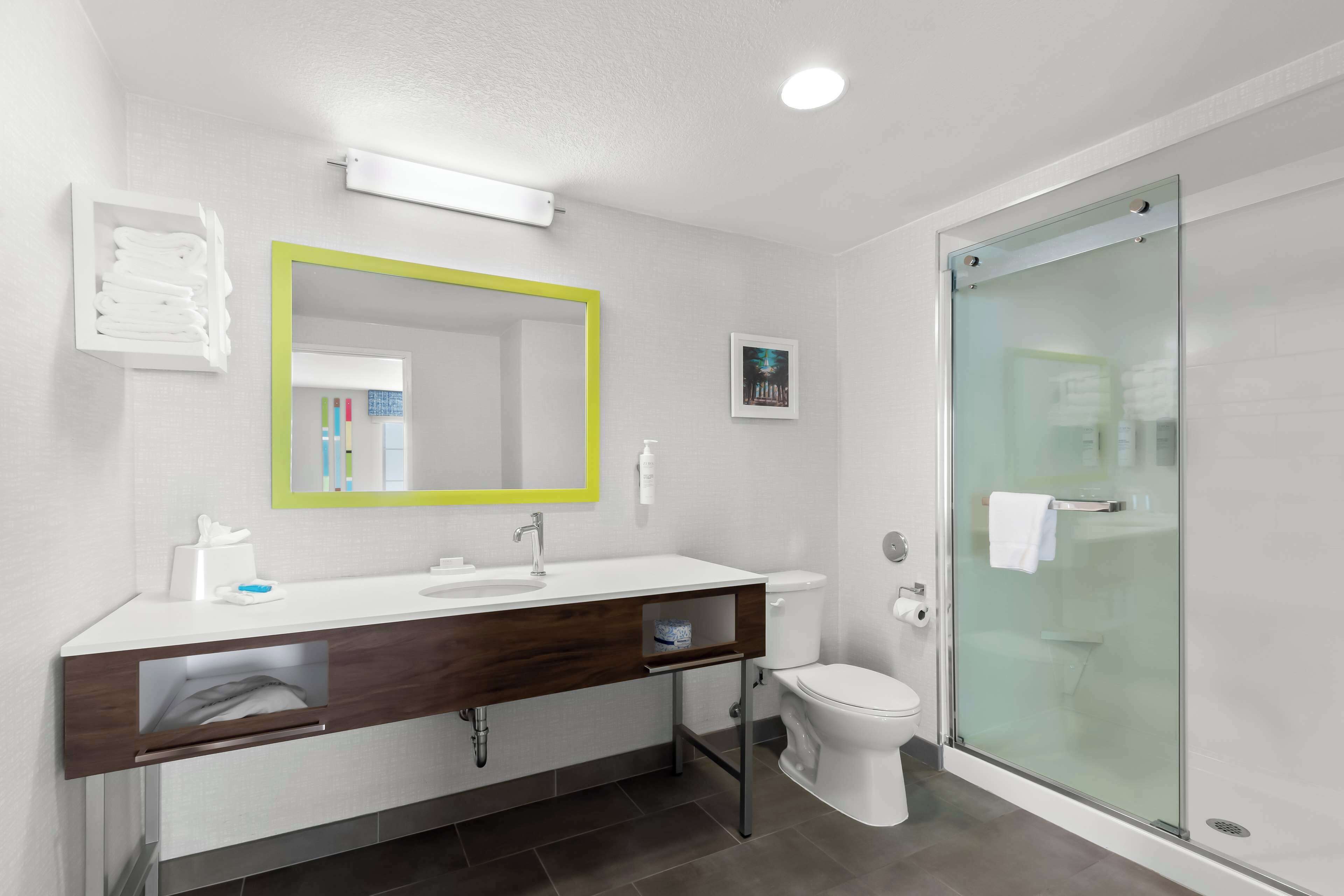 Une salle de bain moderne avec un lavabo blanc, un miroir avec un cadre jaune, des toilettes et une douche en verre.