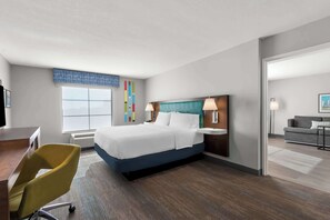 A modern hotel room with a large bed, a desk, a chair, and a sofa.
