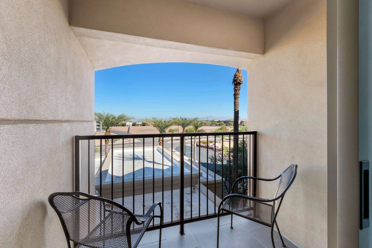 Un balcon avec deux chaises, une balustrade et une vue sur un parking et un paysage lointain.