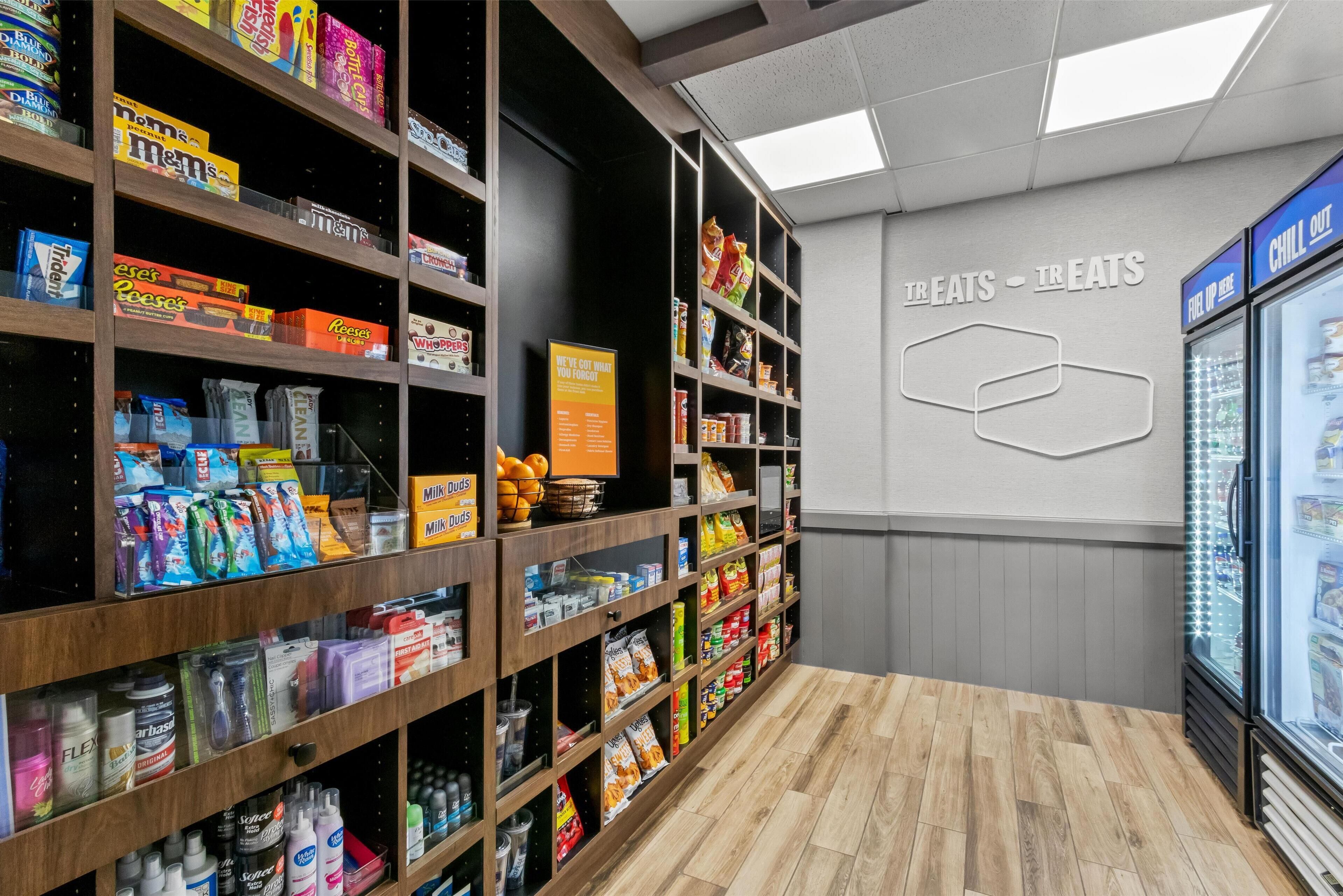 Un espace dédié aux collations et aux boissons, avec des étagères remplies de divers produits, un panneau indiquant un espace « détente » et un autre panneau fixé au mur sur lequel on peut lire « GOURMANDISES – GOURMANDISES ».