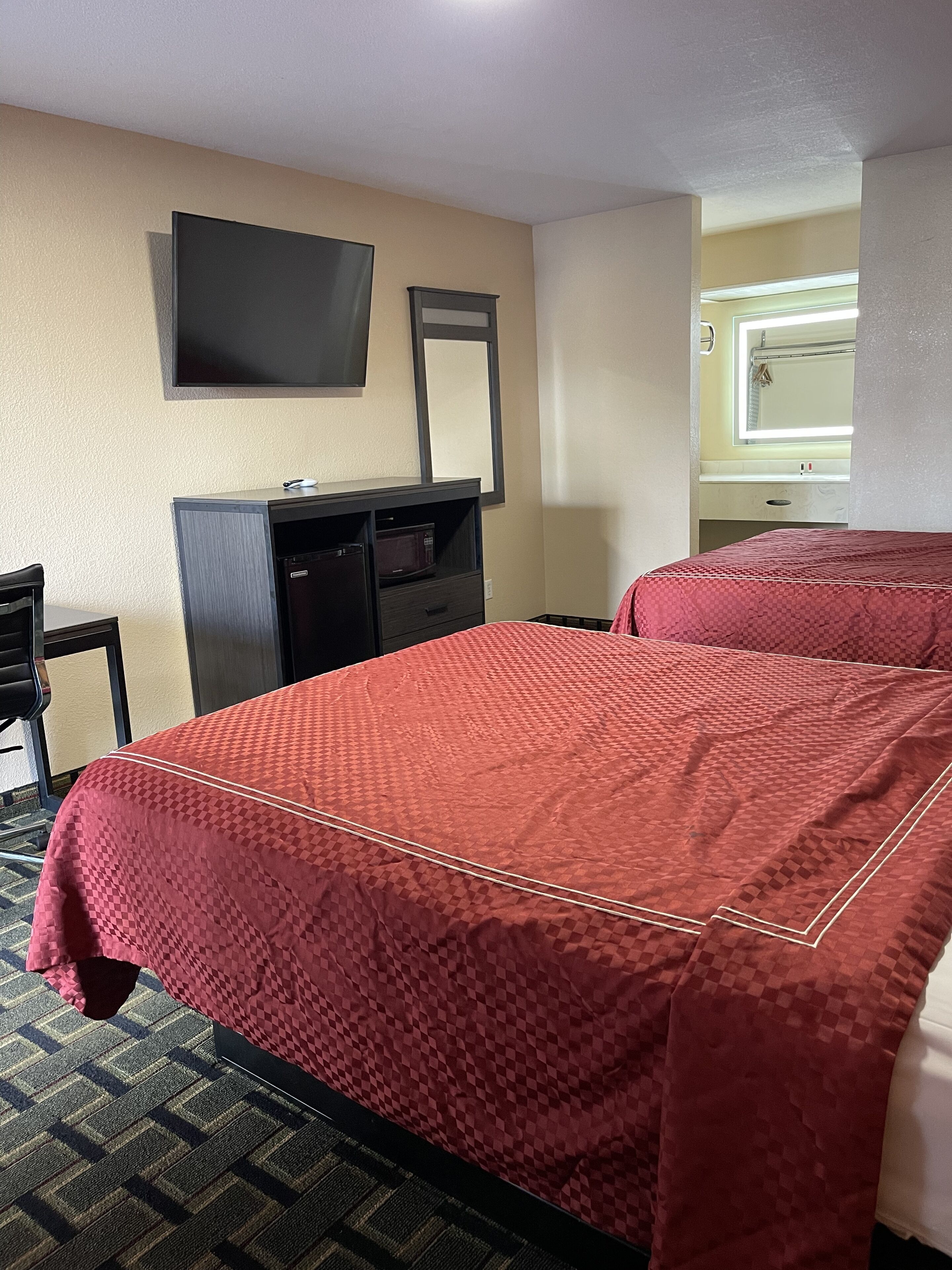 A hotel room with two beds, a desk, a television mounted on the wall, and a window with a view of the outside.
