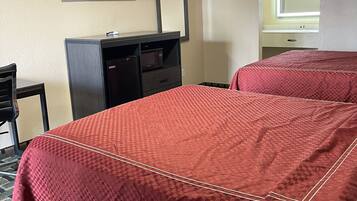 A hotel room with two beds, a desk, a television mounted on the wall, and a window with a view of the outside.