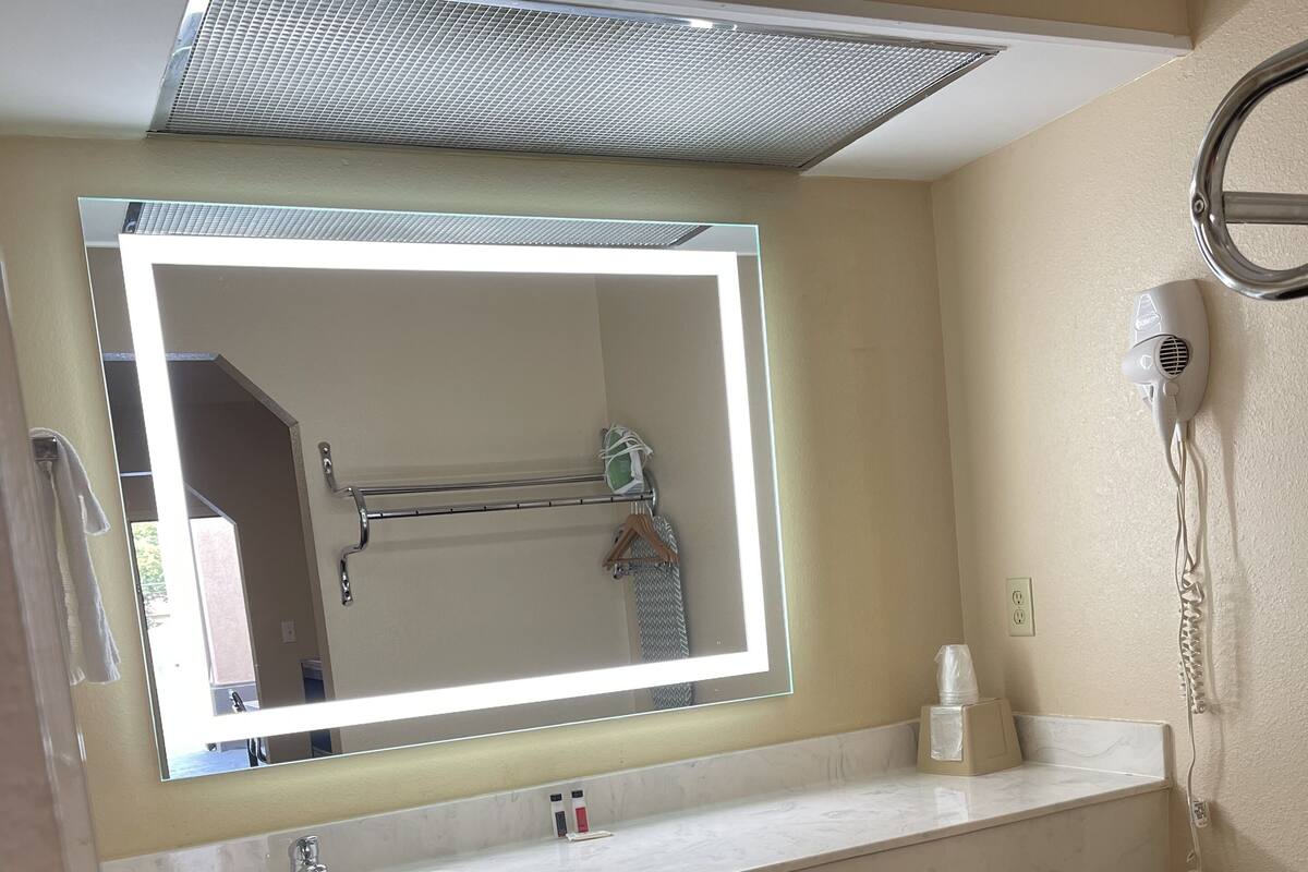 Ein Badezimmer mit großem Spiegel, Waschbecken, Handtuchhalter, Fön und Mülleimer.