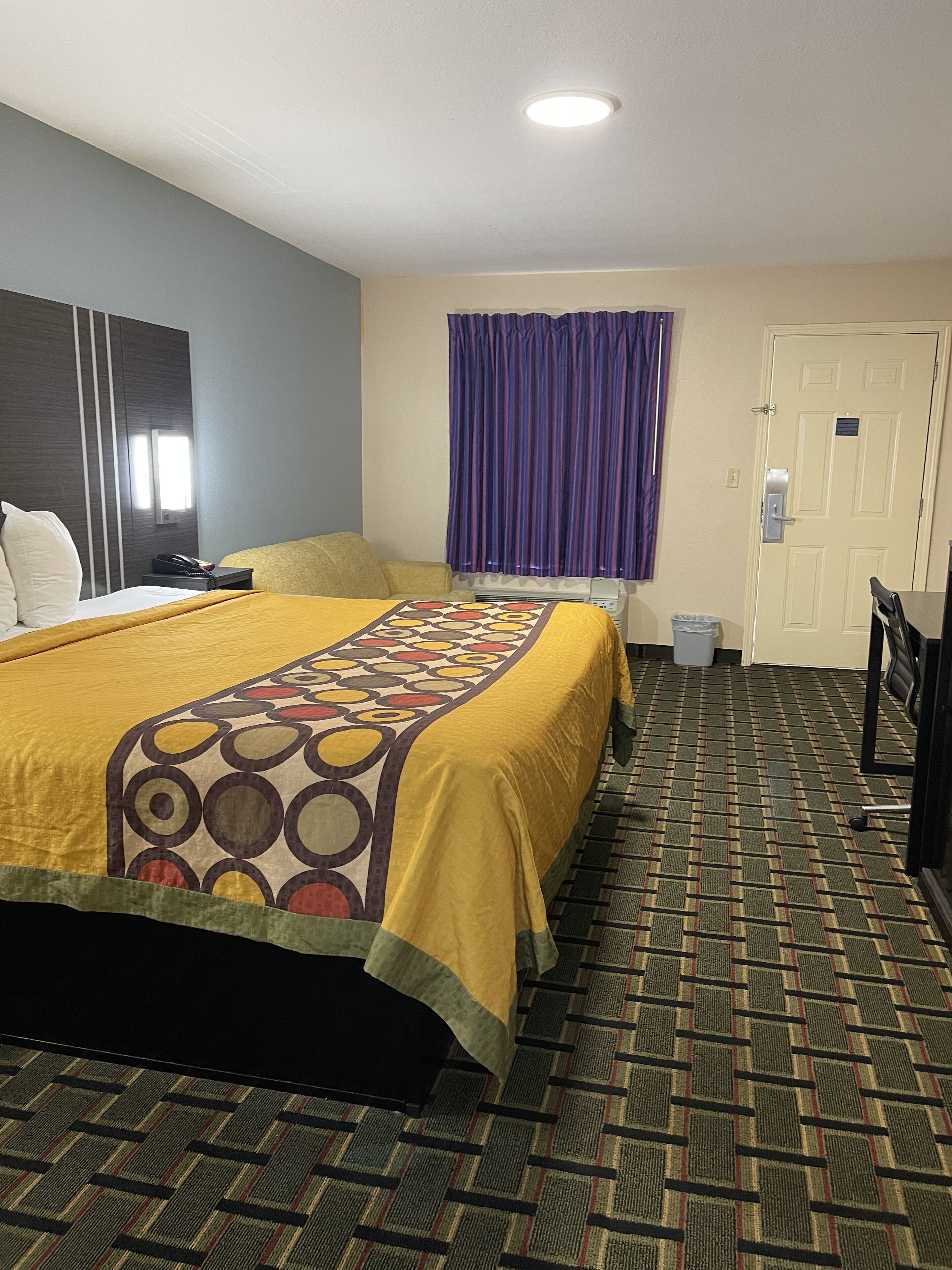 Una habitación de hotel con cama, escritorio, silla, ventana con cortinas y puerta.