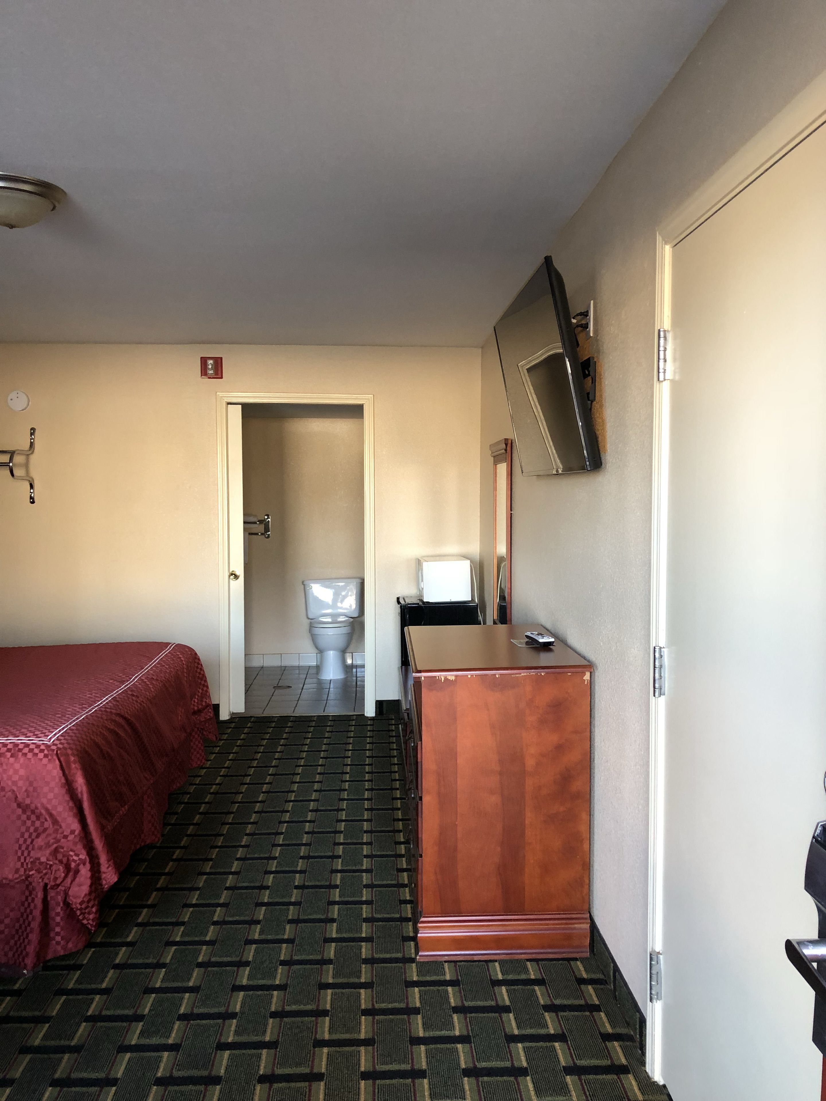 Hotellihuone, jossa on sänky, työpöytä, televisio ja kylpyhuone, jotka näkyv ät avoimesta ovesta.
