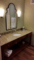 Un baño con lavamanos de encimera de granito, un espejo con marco decorativo y dos luces empotradas en la pared.