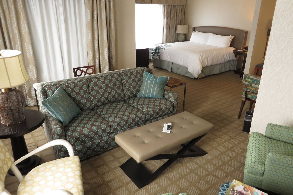 A hotel room with a sofa, a small table with a lamp, a bed, and a chair.
