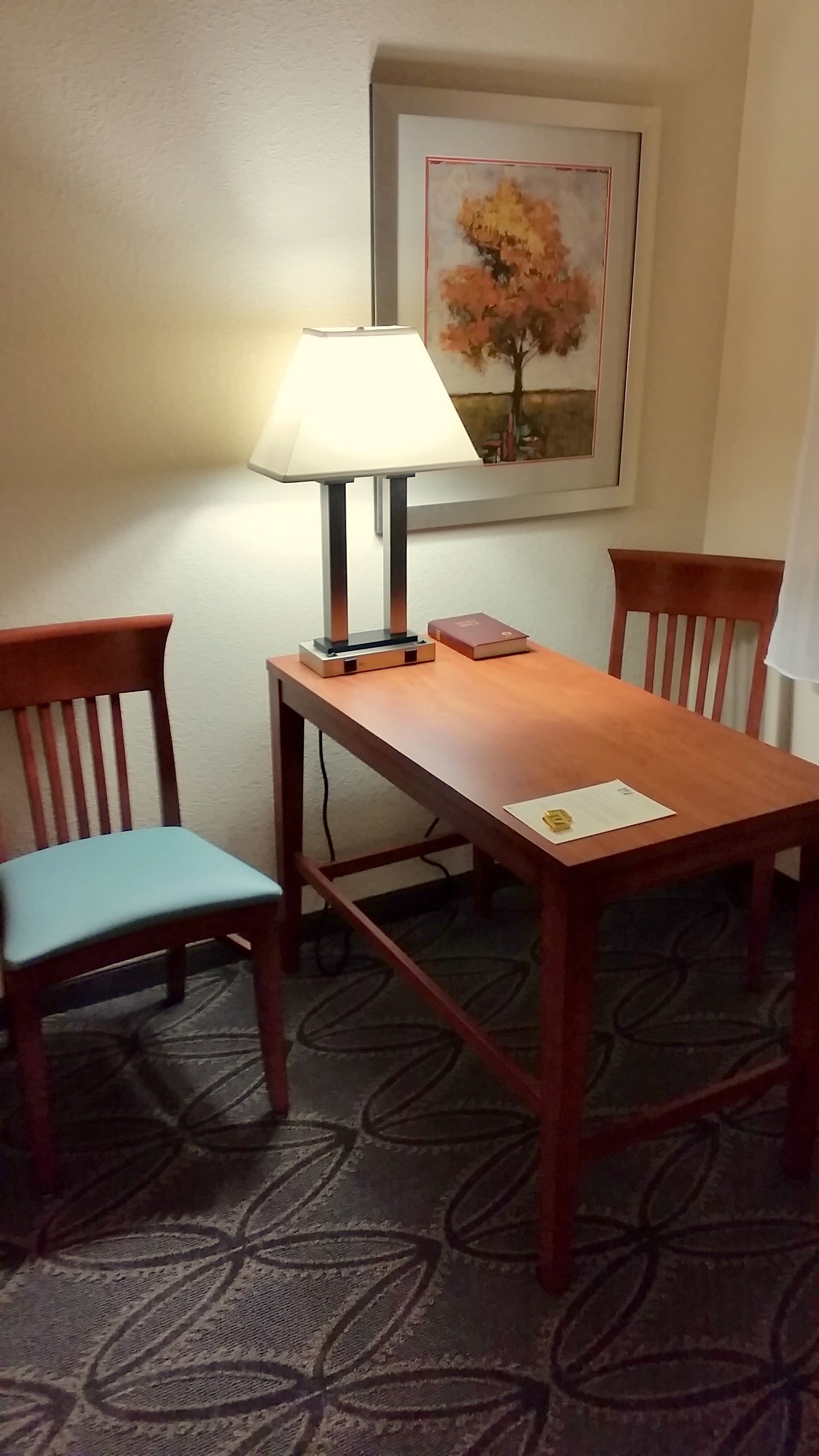 A small dining area with a table, two chairs, a lamp, and a framed picture on the wall.