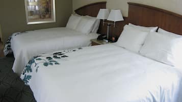 A hotel room with two beds, each with white linens and floral patterns, a nightstand with a lamp, and a framed picture on the wall.