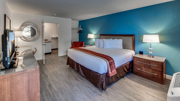 A hotel room with a large bed, bedside tables, a desk, and a mirror. - Angels Inn (Angels Camp)