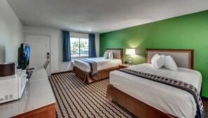 A hotel room with two beds, a TV, a desk with a computer, and a window with curtains.