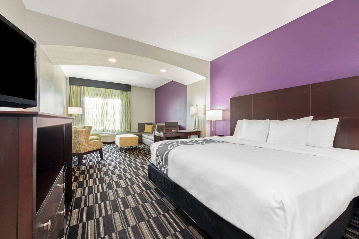 Ein Hotelzimmer mit einem großen Bett, einem Schreibtisch, einem Stuhl und einem Fernseher.