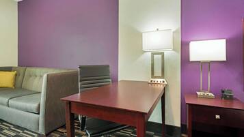 A hotel room with a grey sofa, a wooden table, two wall-mounted lamps, and a small bedside table with a phone.