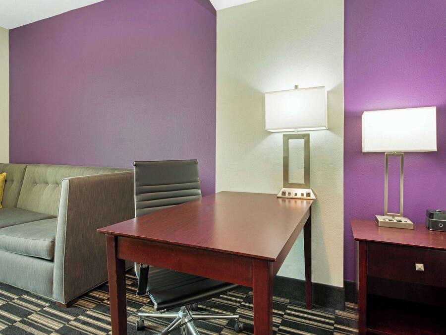 A hotel room with a grey sofa, a wooden table, two wall-mounted lamps, and a small bedside table with a phone.