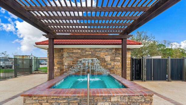 Una piscina de piedra con cascada, rodeada por una pérgola de madera y un muro de ladrillo.