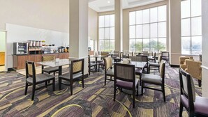 Un amplio comedor de hotel con múltiples mesas y sillas, una barra central con dispensadores de alimentos y bebidas, y grandes ventanales que ofrecen vistas al exterior.