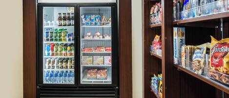 Een gekoelde vitrine gevuld met drankjes en snacks, naast planken met verpakte producten.