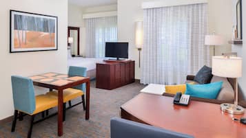 A hotel room with a bed, a TV, a desk with a chair, a lamp, and a painting on the wall.
